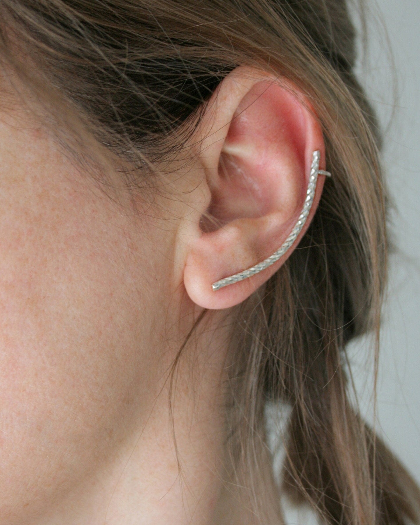 Close-up of an ear wearing a silver hoop earring with a neutral background