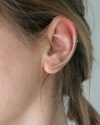 Close-up of an ear wearing a silver hoop earring with a neutral background