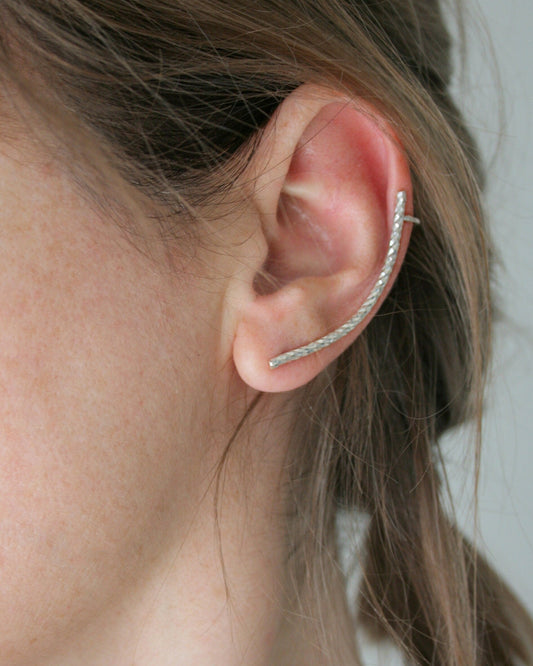 Close-up of an ear wearing a silver hoop earring with a neutral background