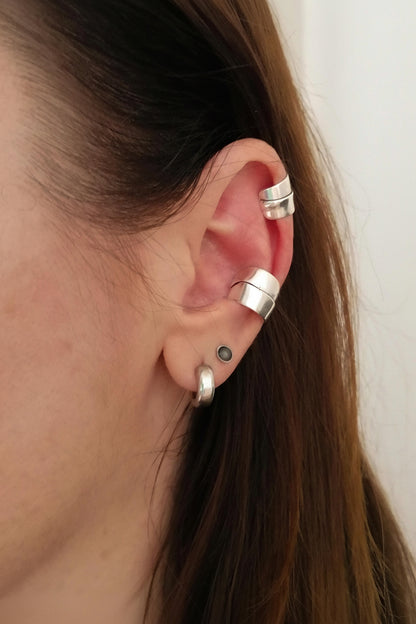 Close-up of an ear with silver earrings and rings on a plain background