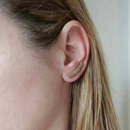 Close-up of an ear wearing a gold earring with a plain background