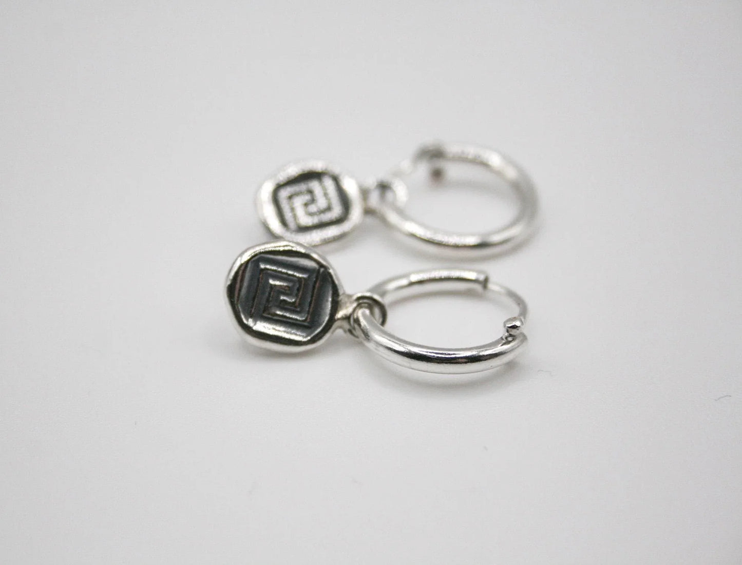 Silver hoop earrings with geometric Greek key pattern charms on white background