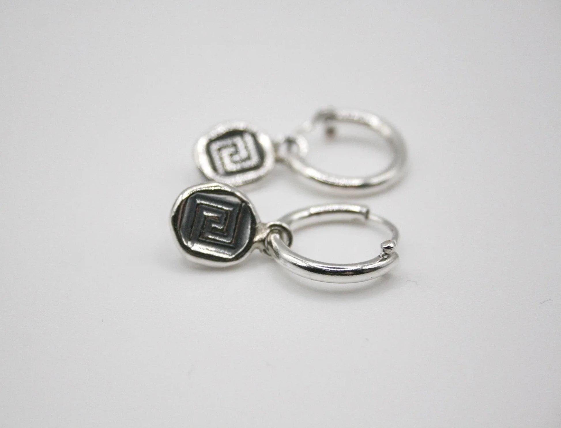 Silver hoop earrings with geometric Greek key pattern charms on white background