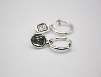 Silver hoop earrings with geometric Greek key pattern charms on white background