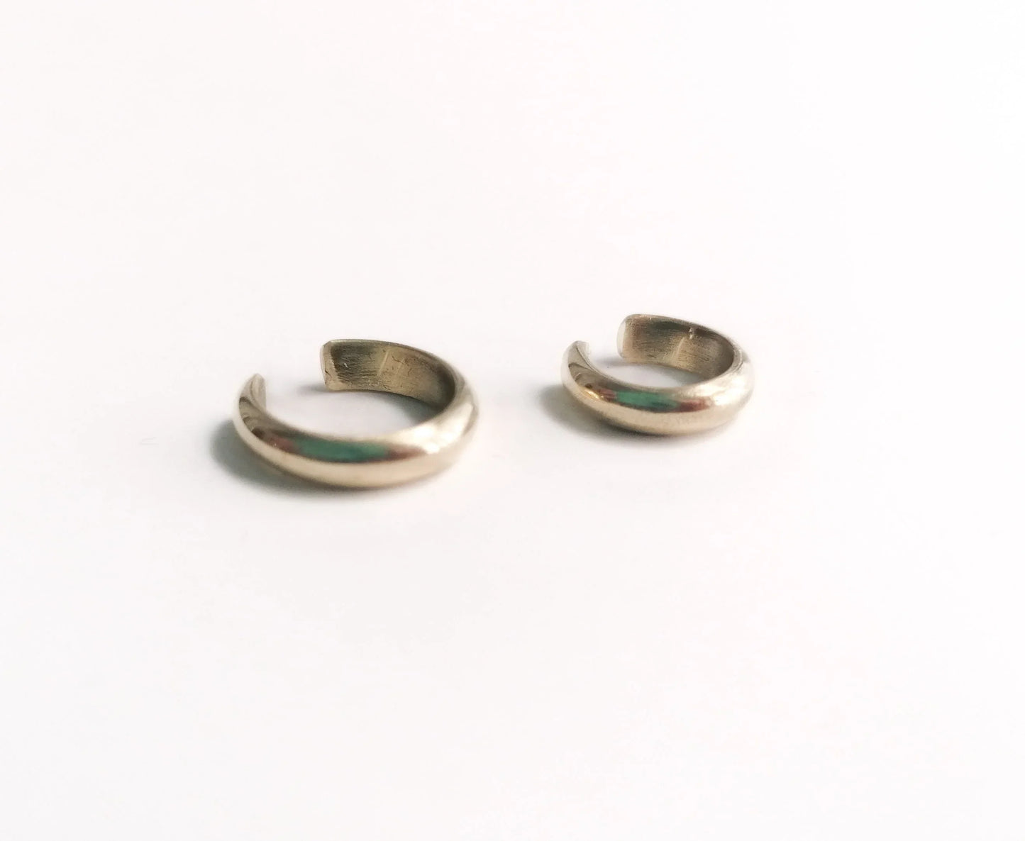 Pair of small silver ear cuffs on white background, minimalist jewelry accessory