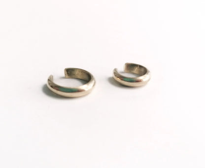 Pair of small silver ear cuffs on white background, minimalist jewelry accessory