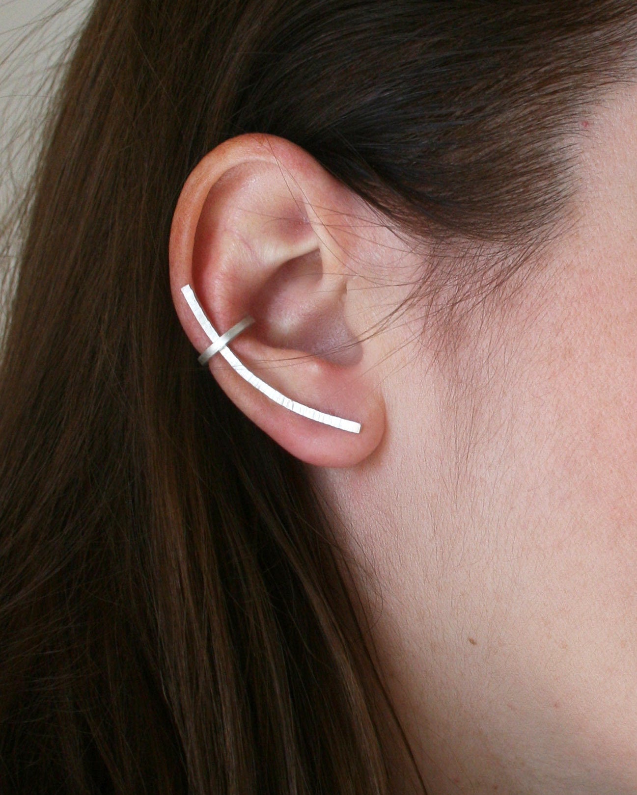 Close-up of an ear wearing a thin silver earring with hair partially covering the face.