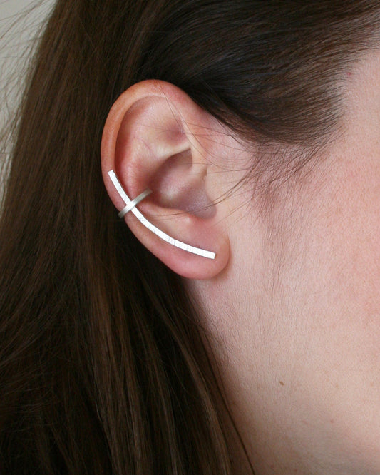 Close-up of an ear wearing a thin silver earring with hair partially covering the face.