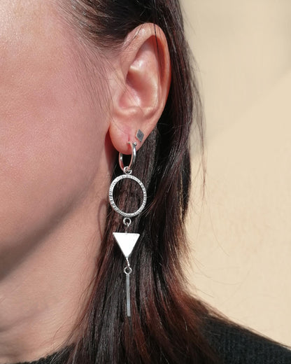 Close-up of an ear wearing a silver earring with a circular and triangular design against a neutral background.