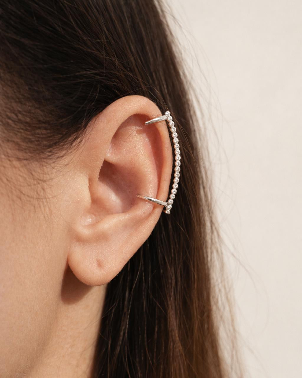 Silver ear cuff worn by a person with dark hair on a neutral background