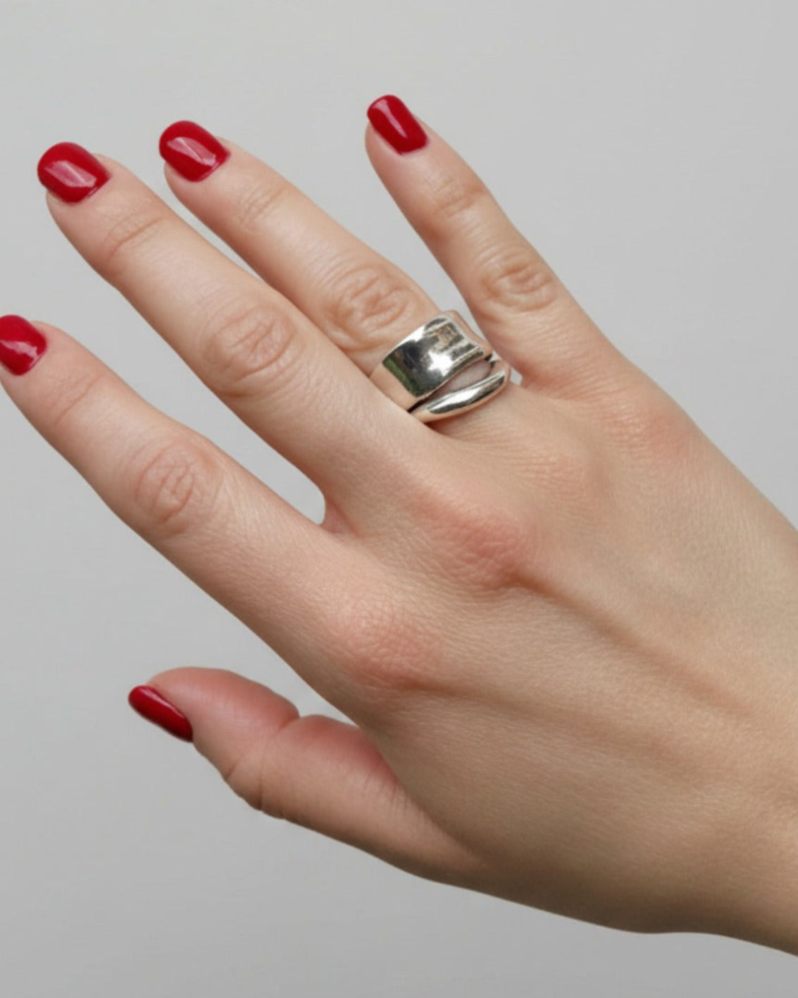 Hand with red nail polish wearing a silver ring on a plain background