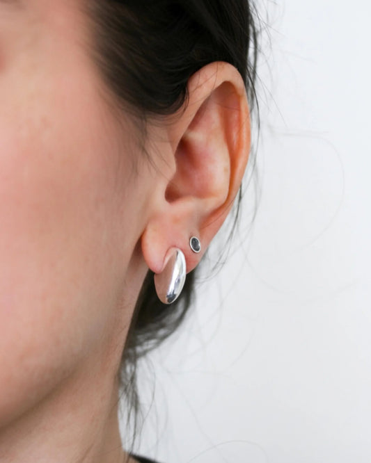 Close-up of an ear wearing a silver earring with a black gemstone on a white background