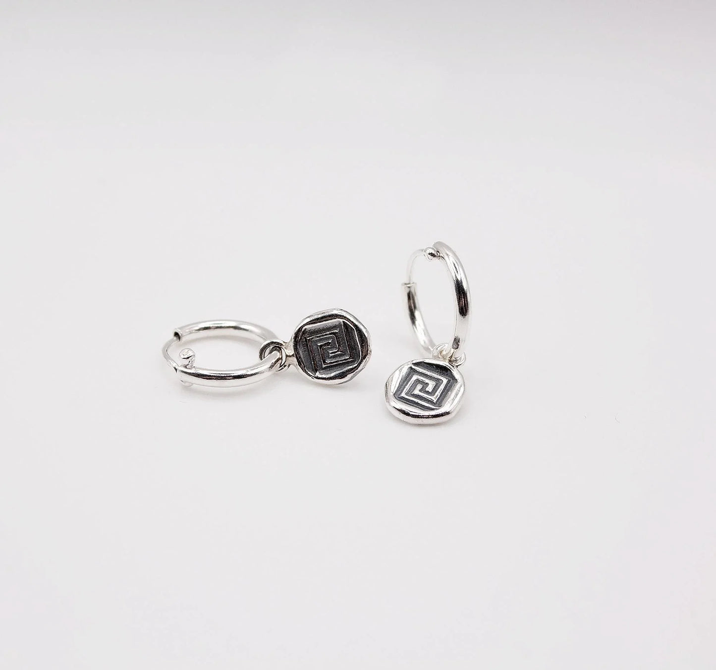 Sterling silver hoop earrings with geometric coin charms on white background