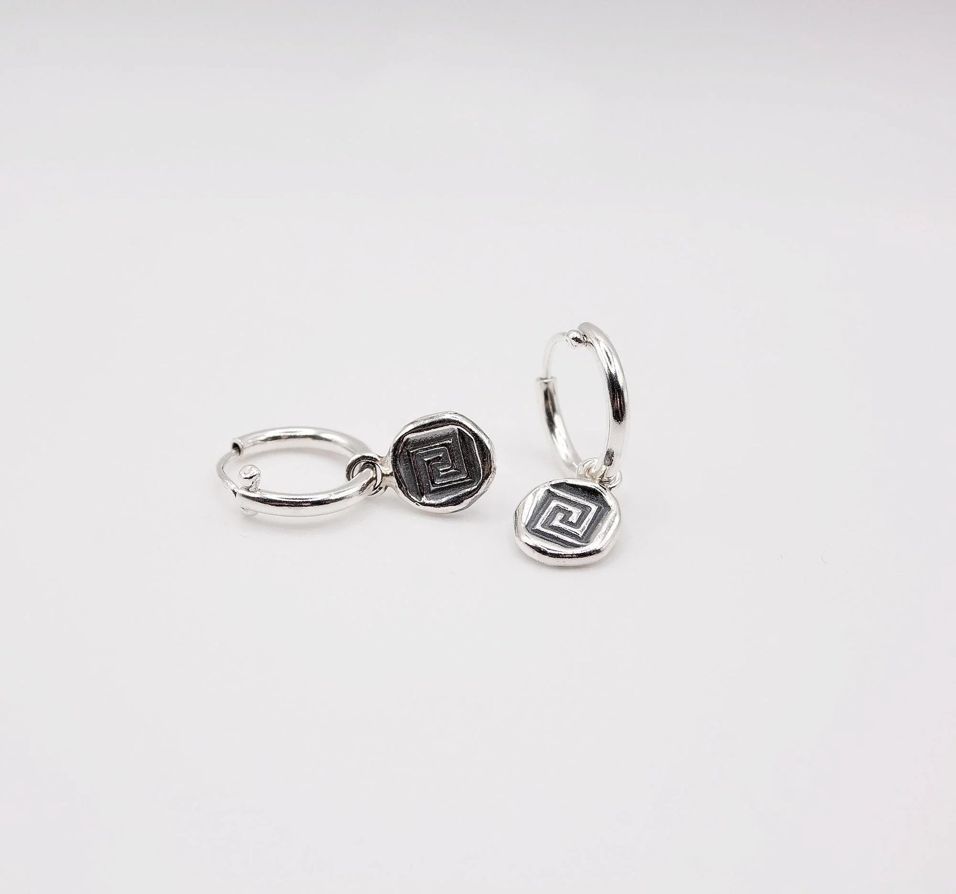 Sterling silver hoop earrings with geometric coin charms on white background