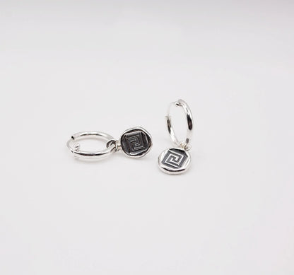 Sterling silver hoop earrings with geometric coin charms on white background