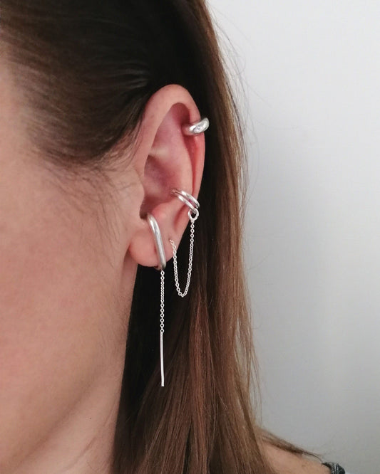 Close-up of a person wearing multiple silver earrings with a plain background