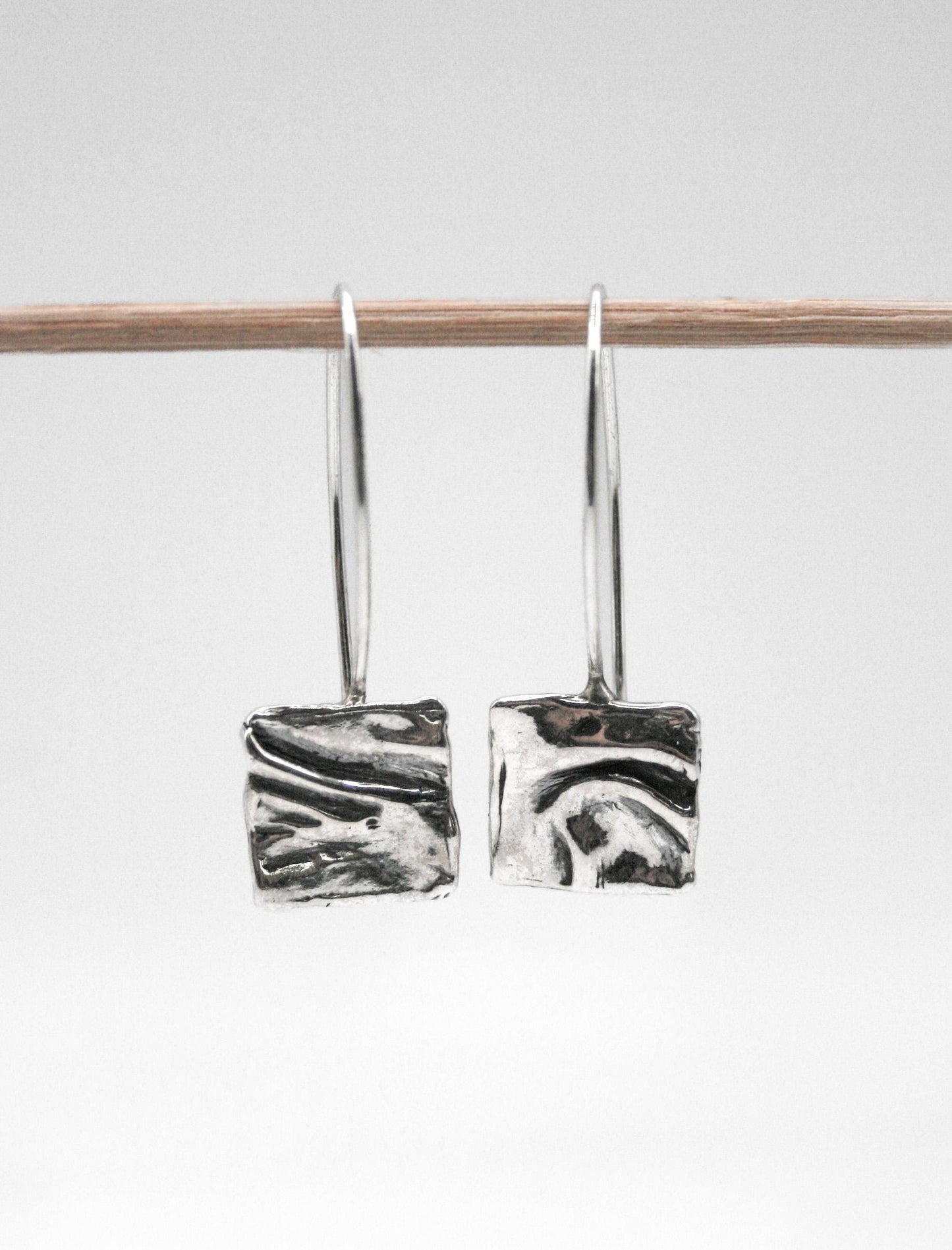 Handcrafted silver square dangle earrings with textured abstract design on white background