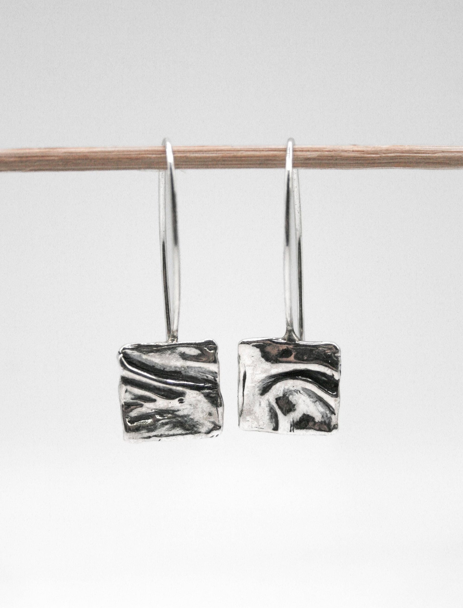 Handcrafted silver square dangle earrings with textured abstract design on white background