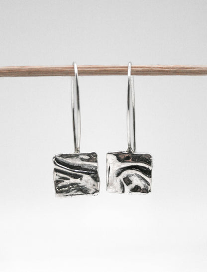 Handcrafted silver square dangle earrings with textured abstract design on white background