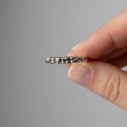 SosyGallery irregular sterling silver band ring with a sculptural, textured organic design held between fingers.