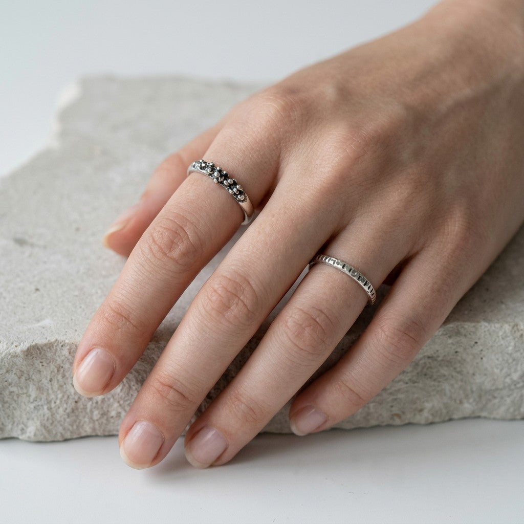 SosyGallery irregular sterling silver stacking rings with sculptural textured details worn on a hand over stone.
